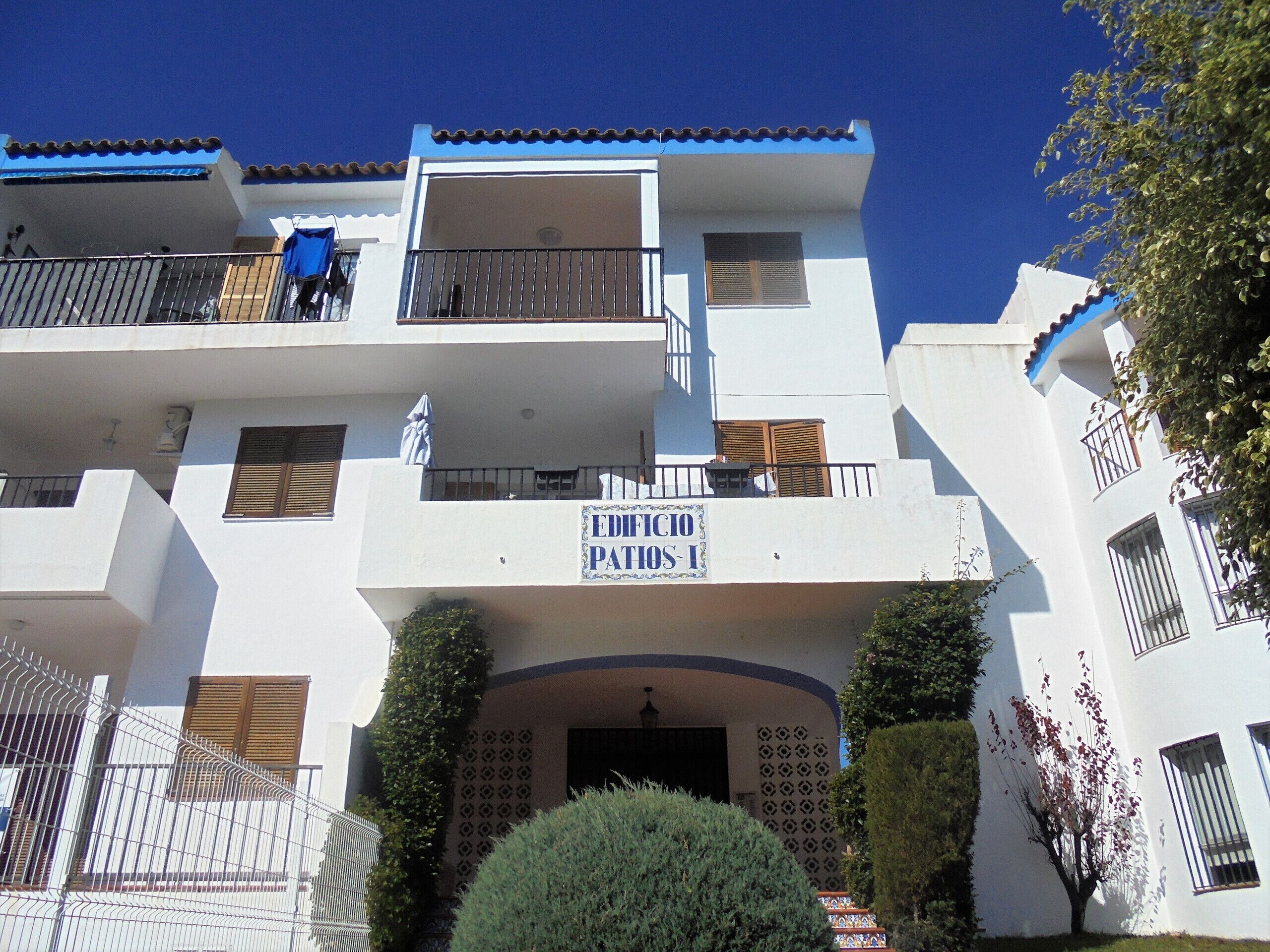 A multi-story building with balconies, a sign reading "EDIFICIO PATRIO," and a gated entrance.