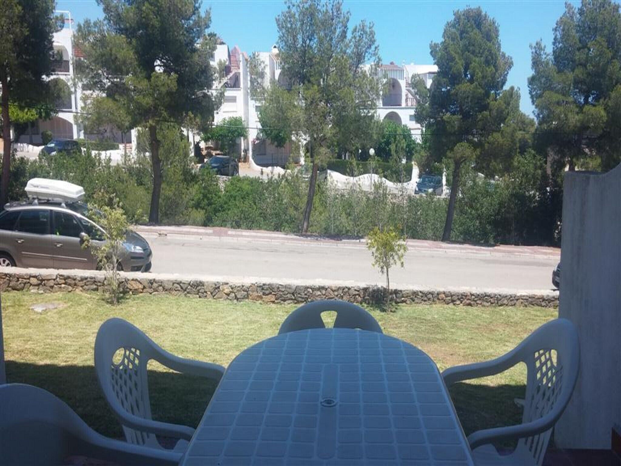 Blick vom Balkon mit Tisch und Stühlen auf eine Straße mit parkenden Autos und Gebäuden im Hintergrund.