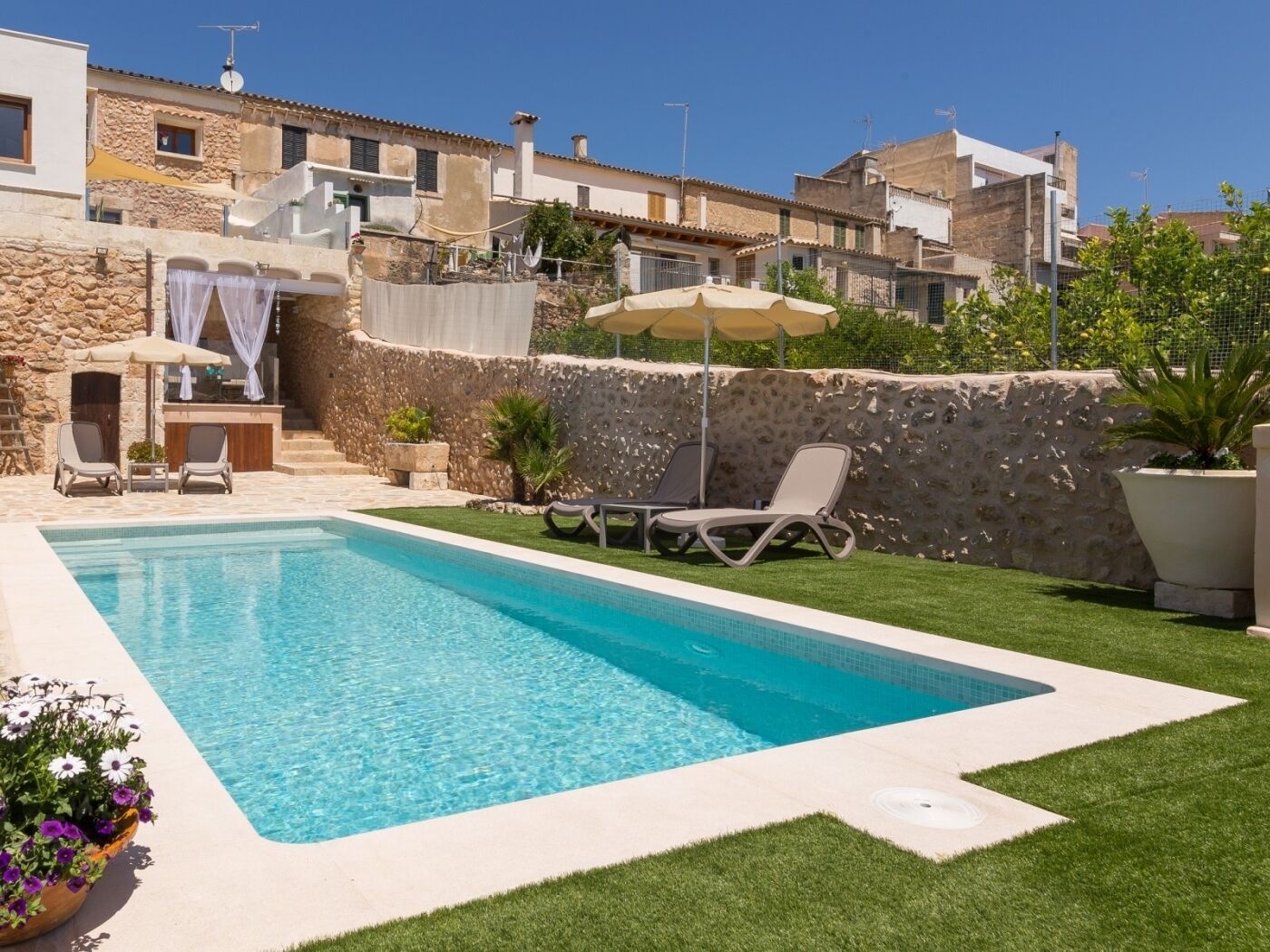 A swimming pool with lounge chairs and umbrellas, surrounded by stone walls and greenery.