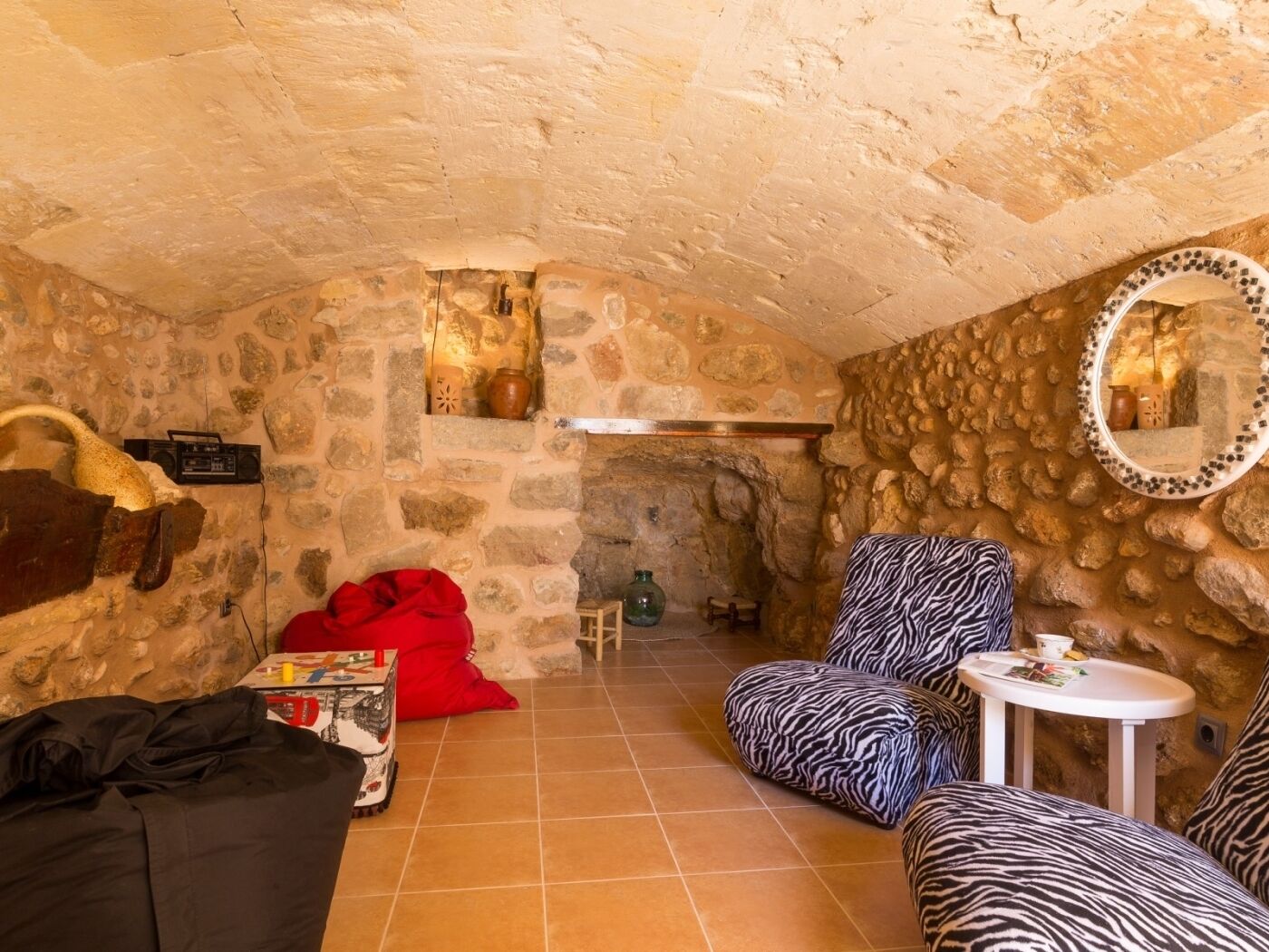 Ein gemütliches Zimmer mit Steinwänden, einem Kamin, einem zebra-gemusterten Sessel, einem roten Sitzsack und einem kleinen runden Tisch mit einer Tasse.