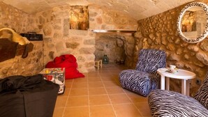 A cozy room with stone walls, a fireplace, a zebra-patterned chair, a red bean bag, and a small round table with a cup. - Casa del Sol - Beautiful town house with pool and views of the countryside (Búger)