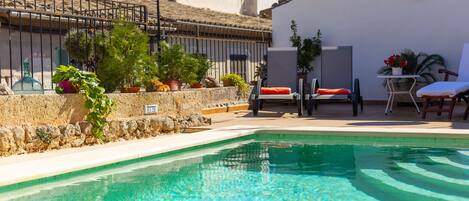 A clear pool with lounge chairs and potted plants.