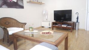 Ein Wohnzimmer mit einer Couch, einem Couchtisch, einem Fernseher, einem Bücherregal und einer Heizung.
