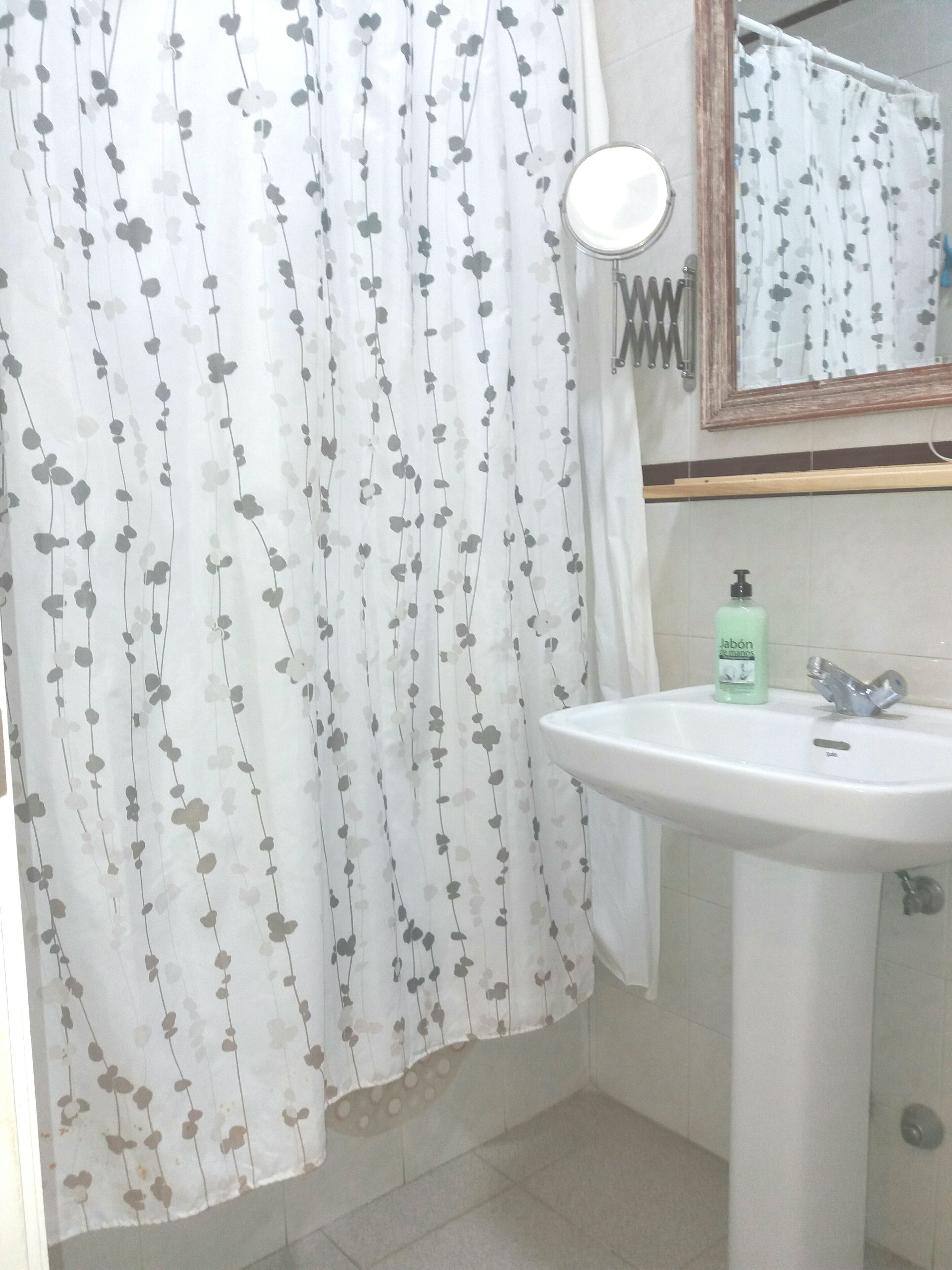 Un baño con lavamanos blanco, espejo y cortina de ducha con estampado floral.