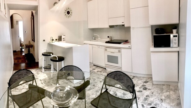 A modern kitchen with white cabinets, a microwave, and a sink. There is a dining area with a glass table and chairs. - Da Vinci Verona, elegant apartment in Borgo Trento, 120 m², parking space (Verona)