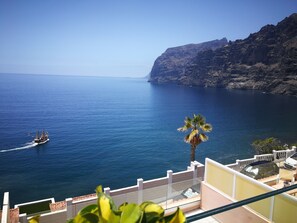 A coastal view with a boat on the water, a palm tree, and a building with a balcony. - Vacation Home: GIANTS AT YOUR FEET  (Santiago del Teide)