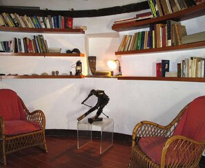 A room with wicker chairs, a clear table, and bookshelves filled with books. - Windmill a little paradise  (Fauglia)