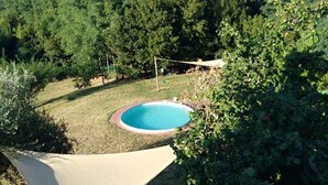En baghave med swimmingpool, omgivet af træer og en hængekøje.