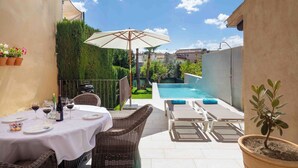 En uteplats med ett bord dukat för måltider, en pool och solstolar.