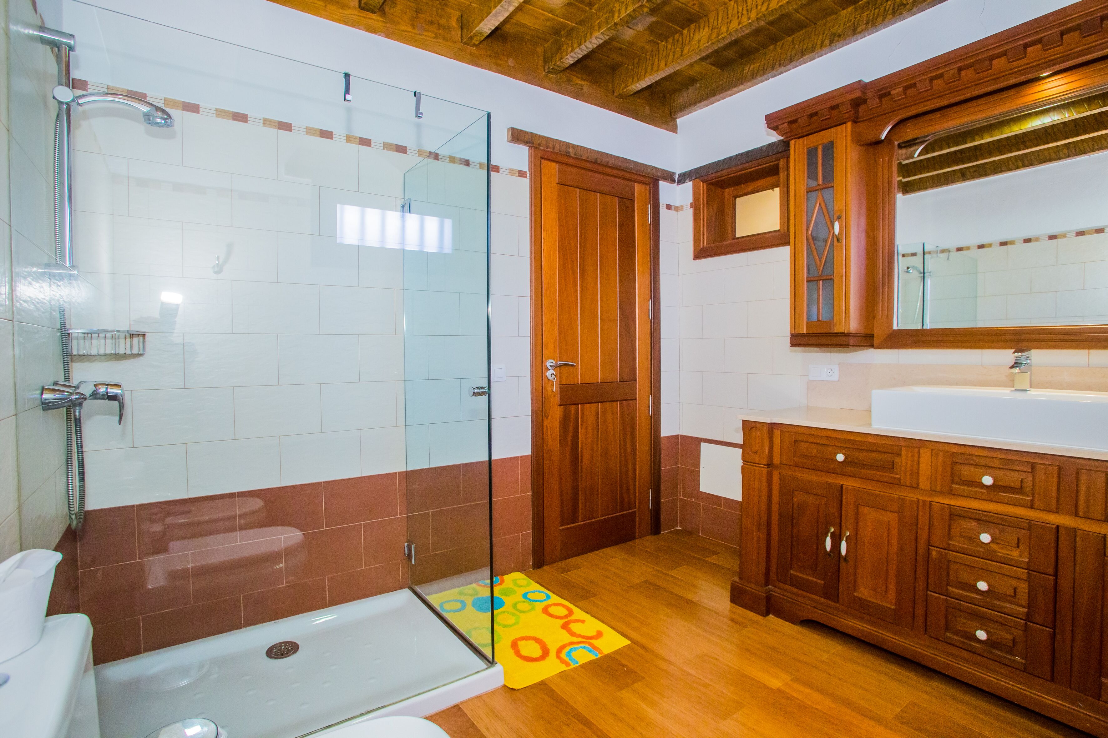A bathroom with a glass shower enclosure, wooden cabinets, and a white sink.