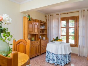 A room with a wooden cabinet, a table with a white tablecloth, and a window with curtains.