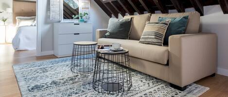 Une chambre mansardée chaleureuse avec un plafond en pente, un canapé avec des coussins, une petite table ronde et un miroir.