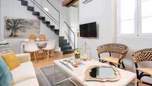 A modern living room with a staircase, a flat-screen TV, and a dining area with wicker chairs. - Genteel Home Trinidad Grund H (Málaga)
