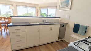 A modern kitchen with a sink, cabinets, and a dishwasher. There is a dining area with chairs and a table visible in the background. - Secluded Coastal Retreat | 107 Acres + 7km Beach (Nepean Bay)