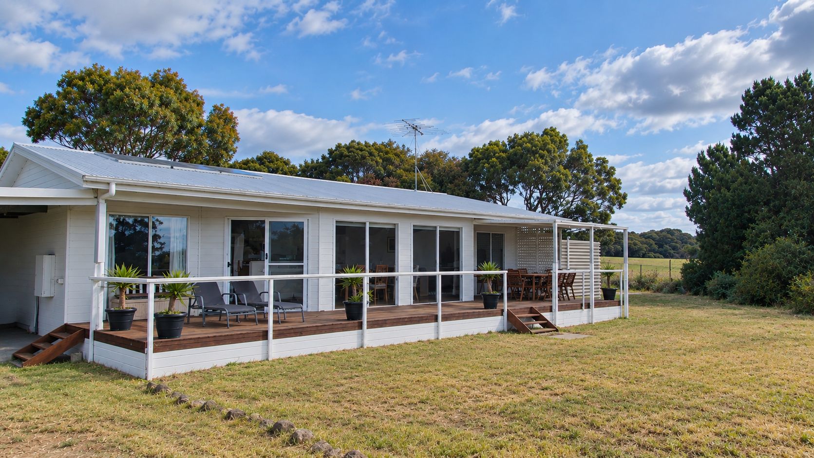 Ein eingeschossiges Haus mit einer Veranda, großen Fenstern und einem Rasen.