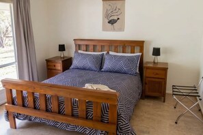 A bedroom with a wooden bed, two bedside tables, a nightstand, a wall-mounted artwork, and a window with curtains.