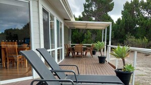 A wooden deck with two lounge chairs, a table, and chairs under a covered area.