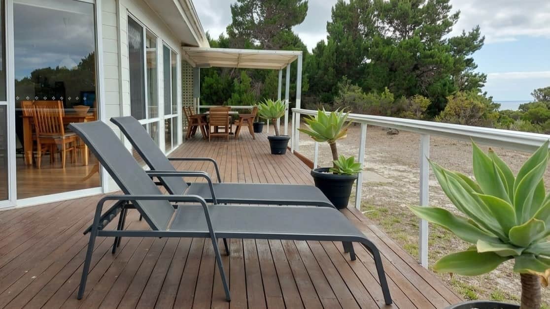 A wooden deck with lounge chairs, a covered seating area, and potted plants.