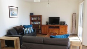 A living room with a sofa, a coffee table, a bookshelf, a television, and speakers.