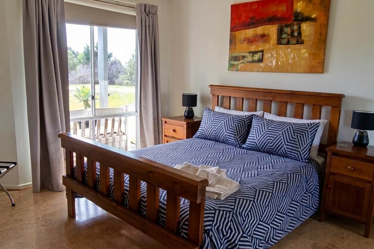 A bedroom with a wooden bed, a nightstand, a lamp, and a window with curtains.