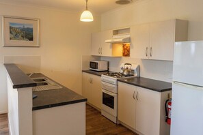 A compact kitchen with white cabinets, a stove, a microwave, and a sink. - Secluded Coastal Retreat | 107 Acres + 7km Beach (Nepean Bay)