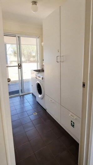 Une buanderie équipée d’un lave-linge, de placards et d’une porte donnant sur un espace extérieur.
