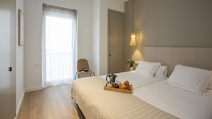 A hotel room with a bed, a bedside table with a lamp, a chair, and a window with curtains.