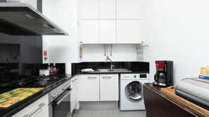 Eine kleine Küche mit Herd, Backofen, Waschmaschine und Kaffeemaschine.
