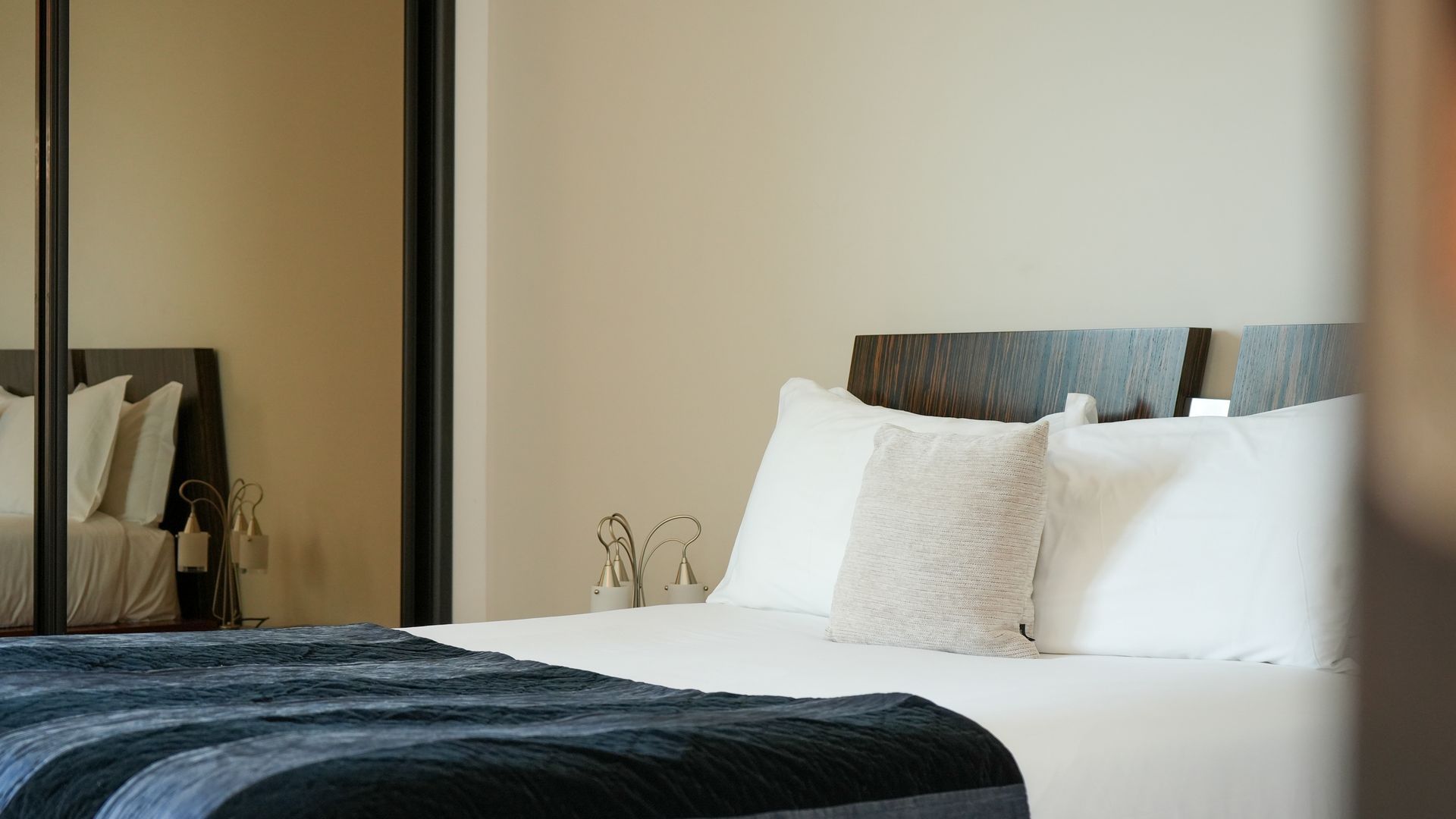 Une chambre d’hôtel avec un grand lit, du linge de lit blanc et un plaid bleu foncé.