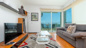 Un salon moderne doté d’un téléviseur à écran plat, d’un canapé, d’une table basse en verre et d’un balcon aménagé avec du mobilier d’extérieur.