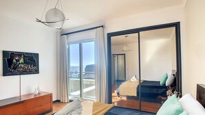 Een moderne hotelkamer met een groot bed, een dressoir, een aan de muur bevestigde televisie en een balkon met uitzicht op de stad.