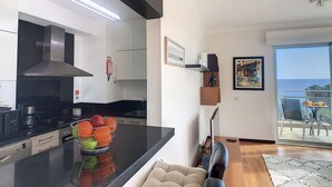 Een moderne keuken met een centraal eiland, een zithoek met een bank en een balkon met uitzicht op zee.