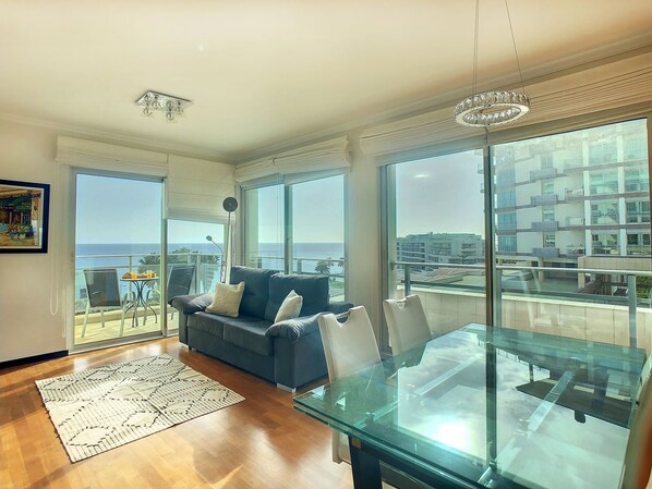 Enjoy ocean views from the large windows in this living room, featuring a glass dining table and comfortable sofa.