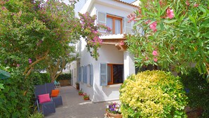 A courtyard with a white building, blue shutters, and outdoor seating. - Casa Alba 159 cosy holiday home with garden, terrace in residential area, barbecue and WiFi (Can Picafort)