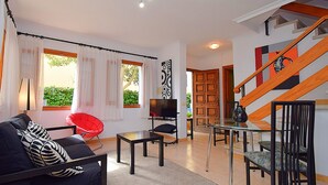 A modern living room with a sofa, coffee table, TV, and a glass dining table. - Casa Alba 159 cosy holiday home with garden, terrace in residential area, barbecue and WiFi (Can Picafort)
