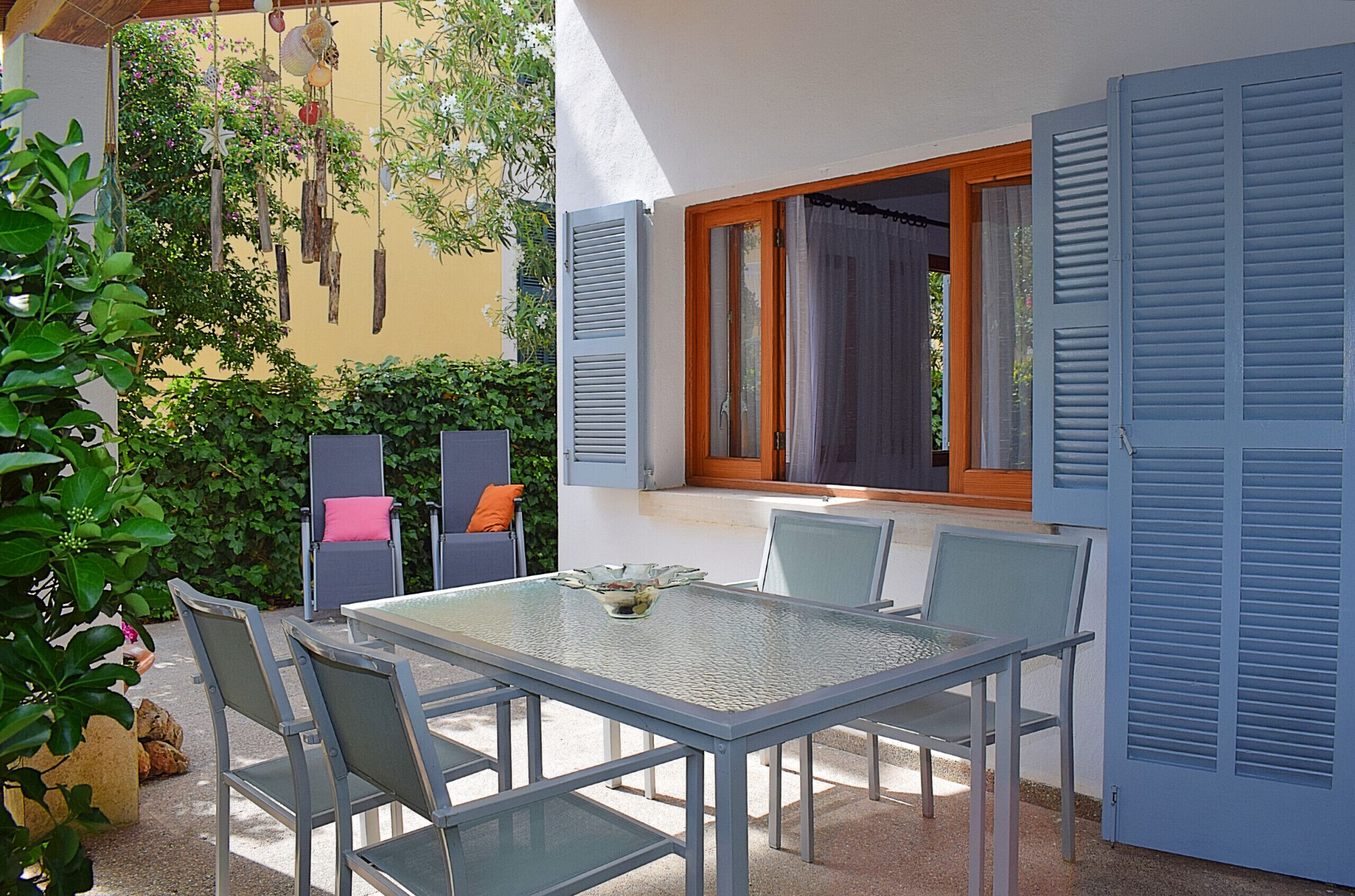 An outdoor patio with a glass table and chairs, a small bowl, and a window with shutters.