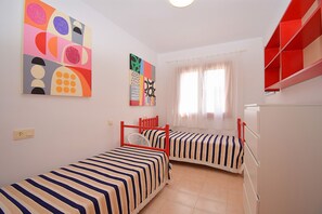 Una habitación con dos camas, una ventana con cortinas y una estantería roja.