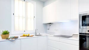 Een moderne keuken met witte kasten, een inbouwoven en een raam met jaloezieën.