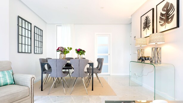 Een moderne eetruimte met een tafel met glazen blad, grijze stoelen en een witte deur op de achtergrond.