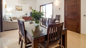 Un coin repas comprenant une table à plateau en verre, des chaises en bois, une plante en pot, un canapé, un téléviseur et une porte en bois.