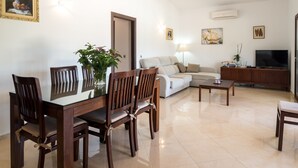 Un salon moderne comprenant une table à manger, des chaises, un canapé, un téléviseur et une plante.