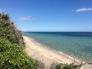 A beach with clear water and a sandy shore, surrounded by greenery. - Giulia terraced house in the shade of pine trees 500 meters from the beach. (PULA)