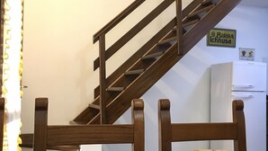 Un escalier avec des rampes en bois, une enseigne indiquant « Birra Ichnusa », et un réfrigérateur à l’arrière-plan.