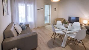 Una sala moderna con un sofá, una mesa de comedor con cubierta de vidrio y sillas.