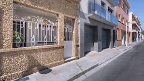 Vista de una calle con un edificio de piedra que presenta puertas metálicas decorativas y ventanas, junto a edificios modernos con balcones.
