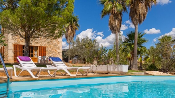 A pool area with white lounge chairs and a stone building in the background. - Banyols - Beautiful villa with pool in Alaró (Alaro)