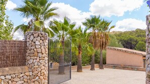 A gated entrance with palm trees, a stone wall, and a building in the background. - Banyols - Beautiful villa with pool in Alaró (Alaro)