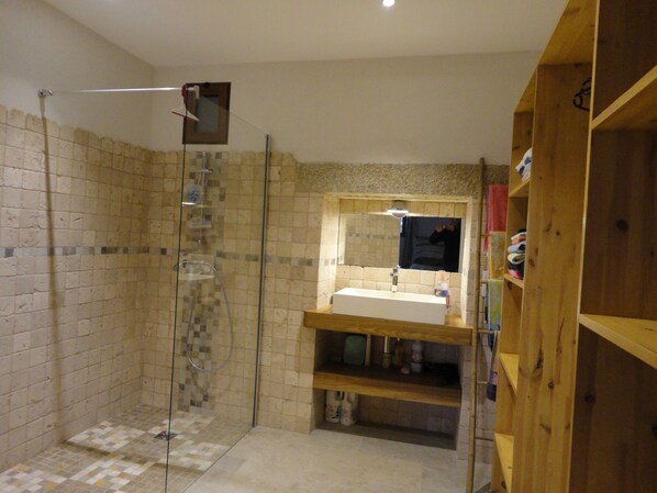 Une salle de bain avec une douche à parois de verre, un lavabo avec un miroir au-dessus et des étagères en bois.