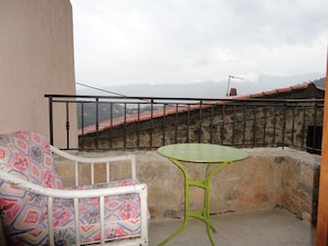 Un balcón con una silla de diseño y una pequeña mesa, con vistas a un paisaje montañoso.