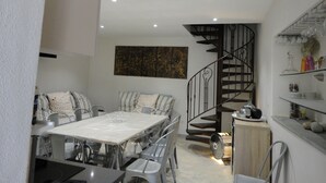 Un espace de salle à manger moderne avec une table à plateau en verre, des chaises en métal et un escalier doté d’une rampe noire.